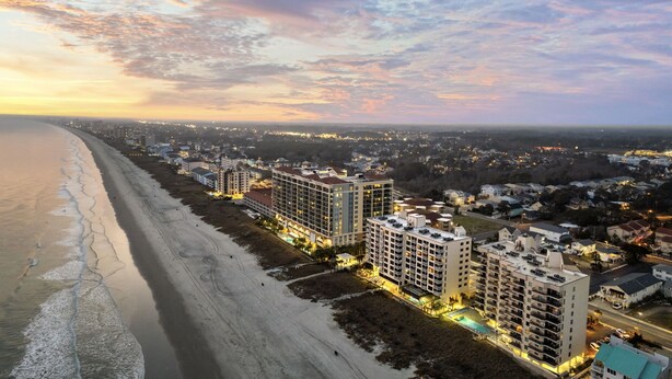Un hôtel situé sur la côte, composé de plusieurs immeubles de grande hauteur, offrant un accès direct à la plage et donnant sur un paysage urbain en arrière-plan.