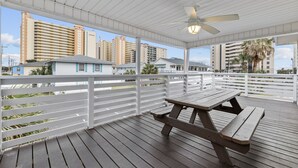 Un espace extérieur abrité, doté d’une table de pique-nique en bois, de rampes blanches et offrant une vue sur de hauts immeubles en arrière-plan.