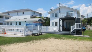 Ein Anwesen am Strand mit einem zweigeschossigen Haus, einer überdachten Veranda und einem eingezäunten Bereich mit einer Bank.
