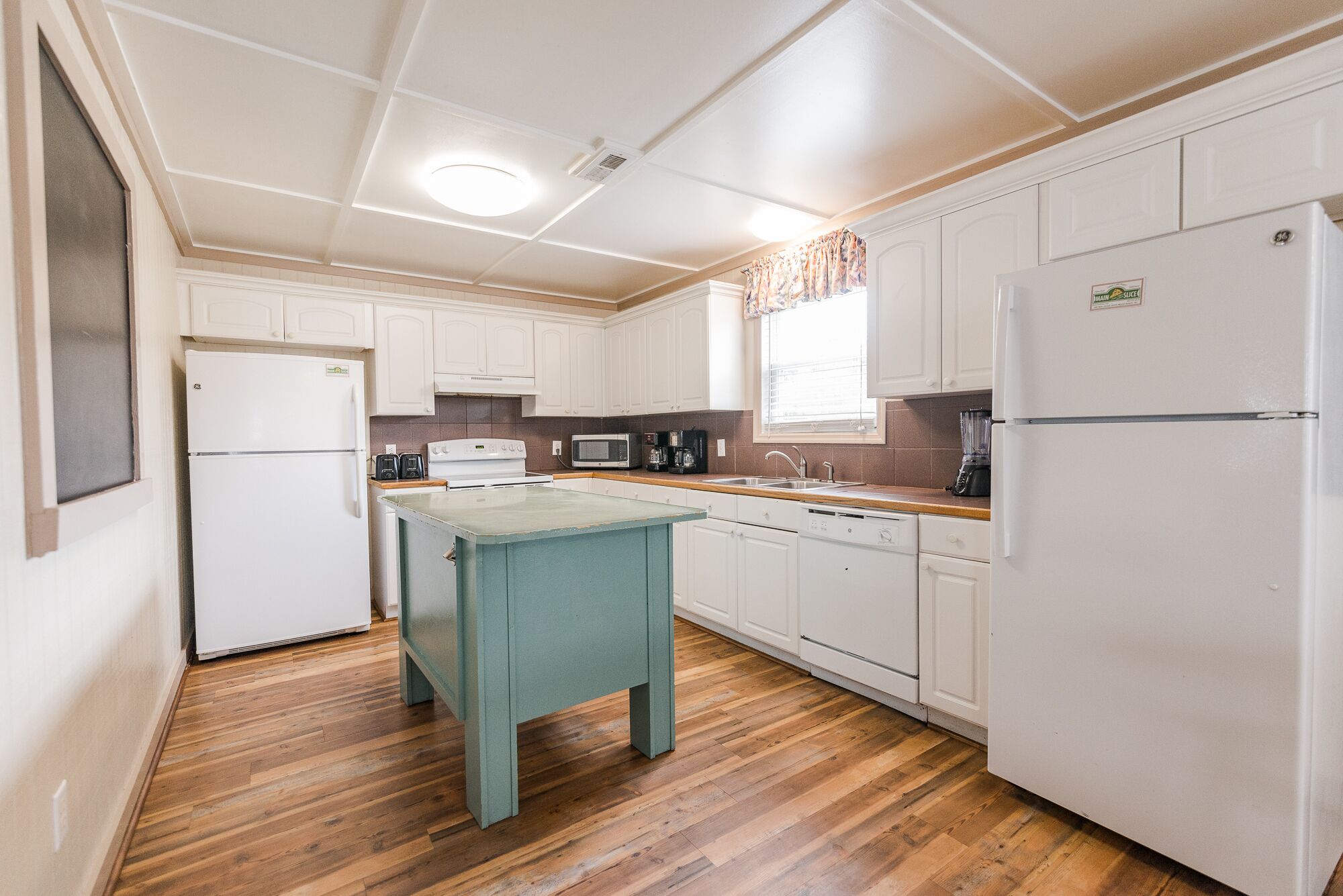 A compact kitchen with white cabinets, a small island table, a refrigerator, a microwave, and a sink.