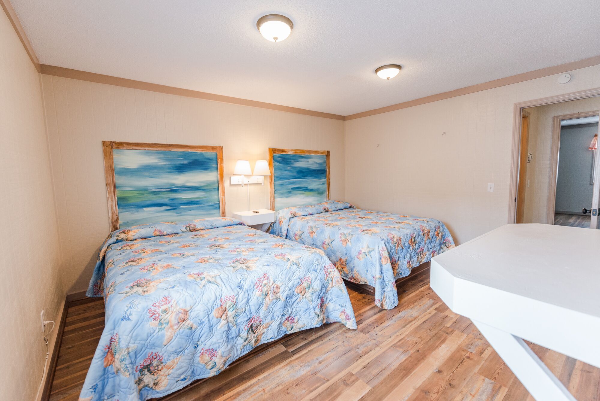 Quarto com duas camas, cada uma com roupa de cama florida, uma mesa branca e duas luminárias fixadas na parede.