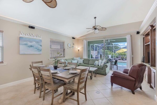 A dining area with a table and chairs, a sofa, a ceiling fan, and a view of the outdoors.