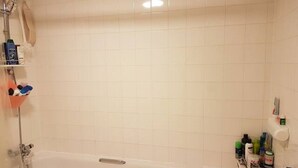 Een badkamer met een badkuip, douche en een plank met toiletartikelen.