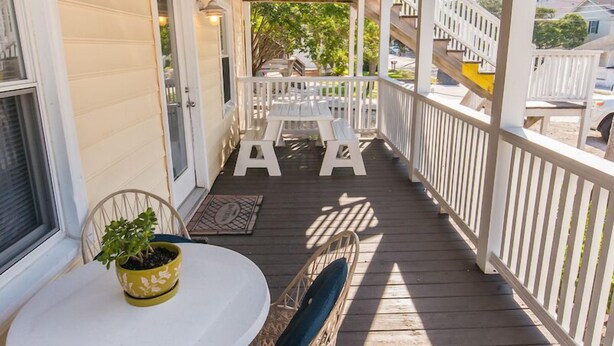 Un espace extérieur abrité doté d’une terrasse en bois, de chaises en osier, d’une table agrémentée d’une plante en pot et d’une rambarde blanche.