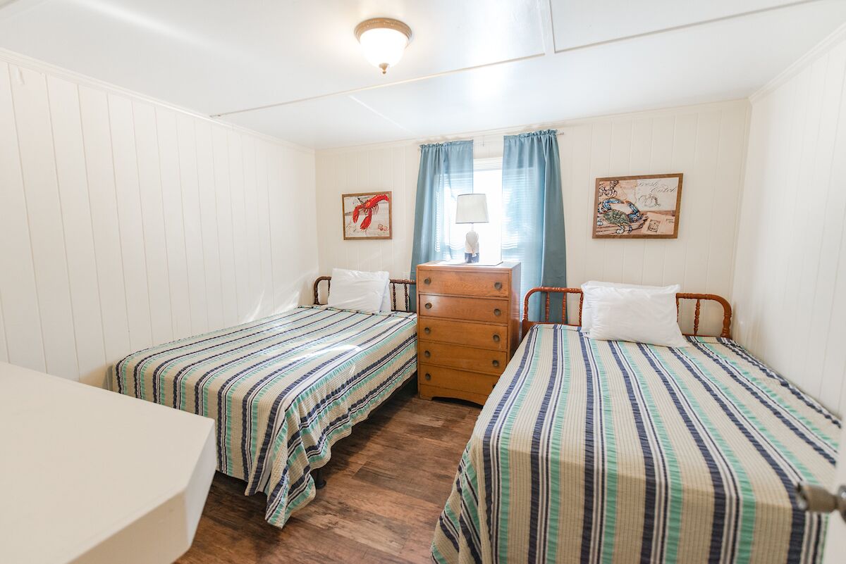 Een kamer met twee enkele bedden, een houten dressoir, een nachtkastje en een raam met gordijnen.
