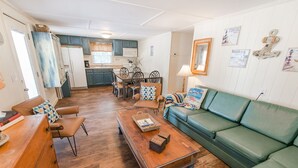 Un salon chaleureux avec un canapé vert, une table basse en bois et un coin repas donnant sur une cuisine en arrière-plan.