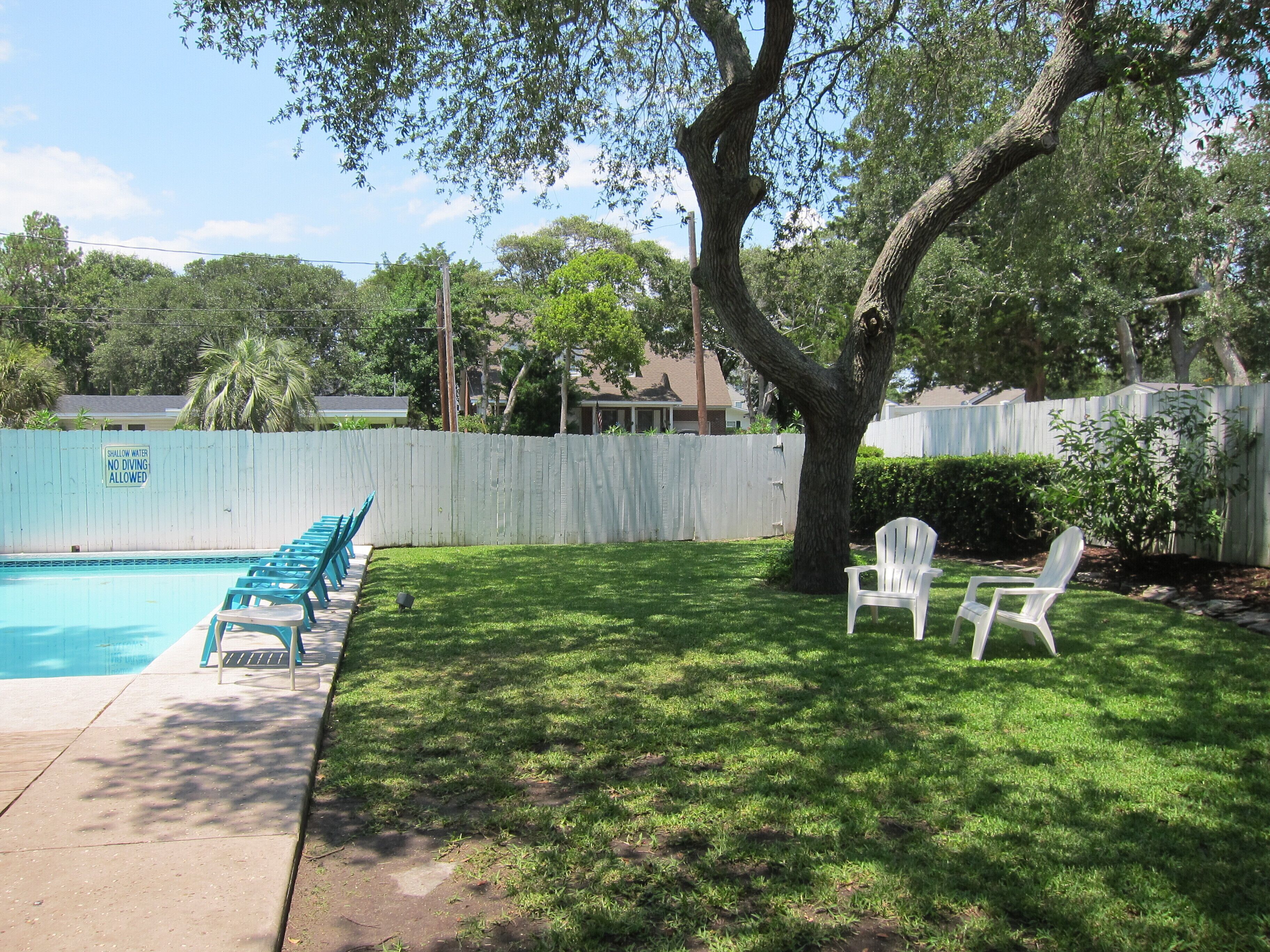 A backyard with a swimming pool, a white fence, and two white chairs.