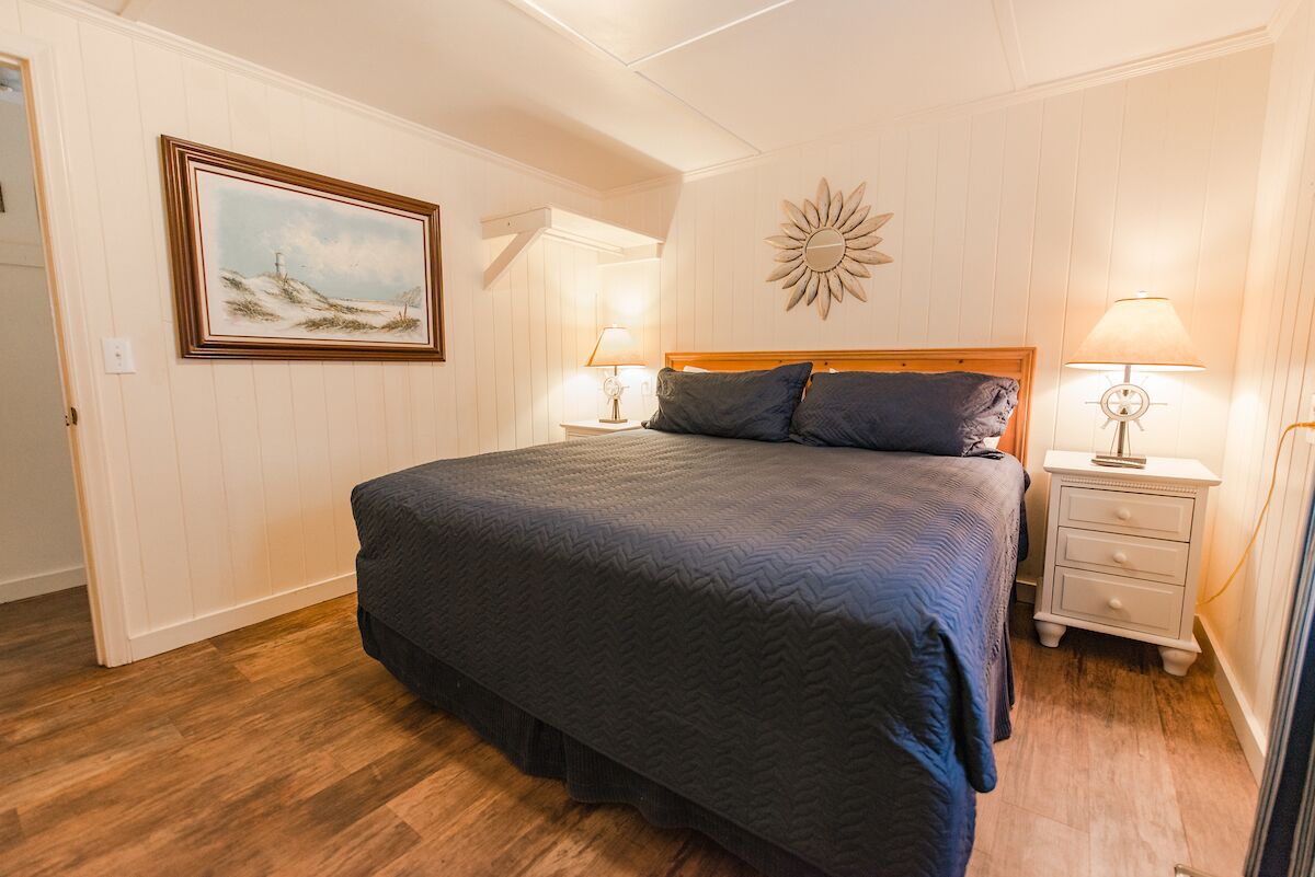 Un dormitorio con una cama grande, dos mesitas de noche con lámparas, un cuadro en la pared y un adorno con forma de sol sobre la cama.