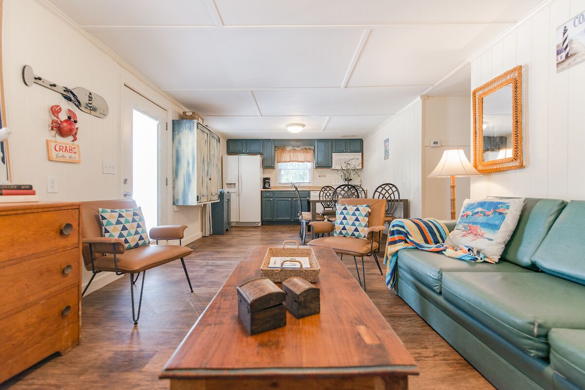 Een gezellige woonkamer met een houten salontafel, een groene bank en een eethoek, met een keuken op de achtergrond.