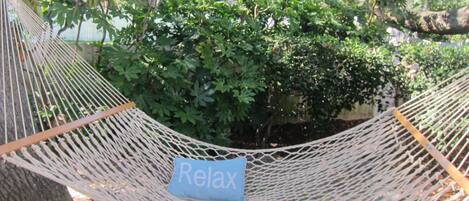 A hammock with a 'Relax' sign, set against a backdrop of dense foliage and a tree trunk.