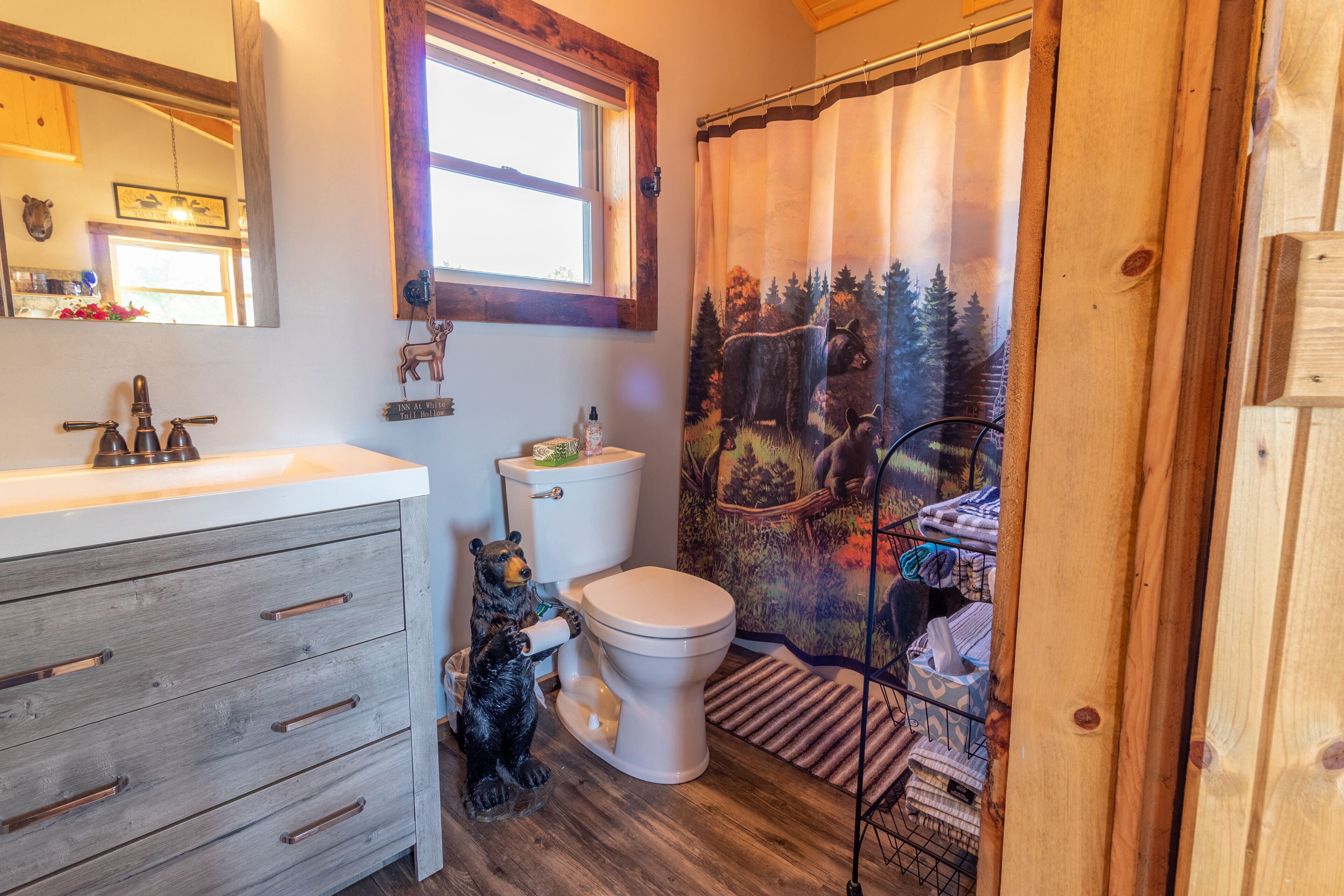 Un baño con tocador de madera, inodoro y decoración de oso.