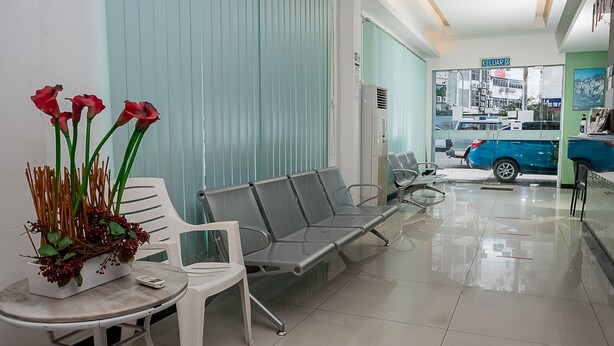 A waiting area with chairs, a table with a vase of flowers, and a blue car parked outside. - OYO 90055 Mansion Inn (Sibu)