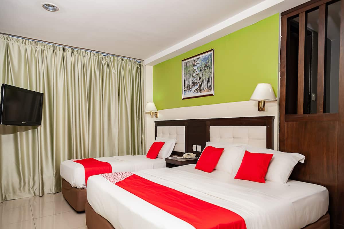 A hotel room with two beds, a flat-screen TV, a painting on the wall, and a green accent wall.