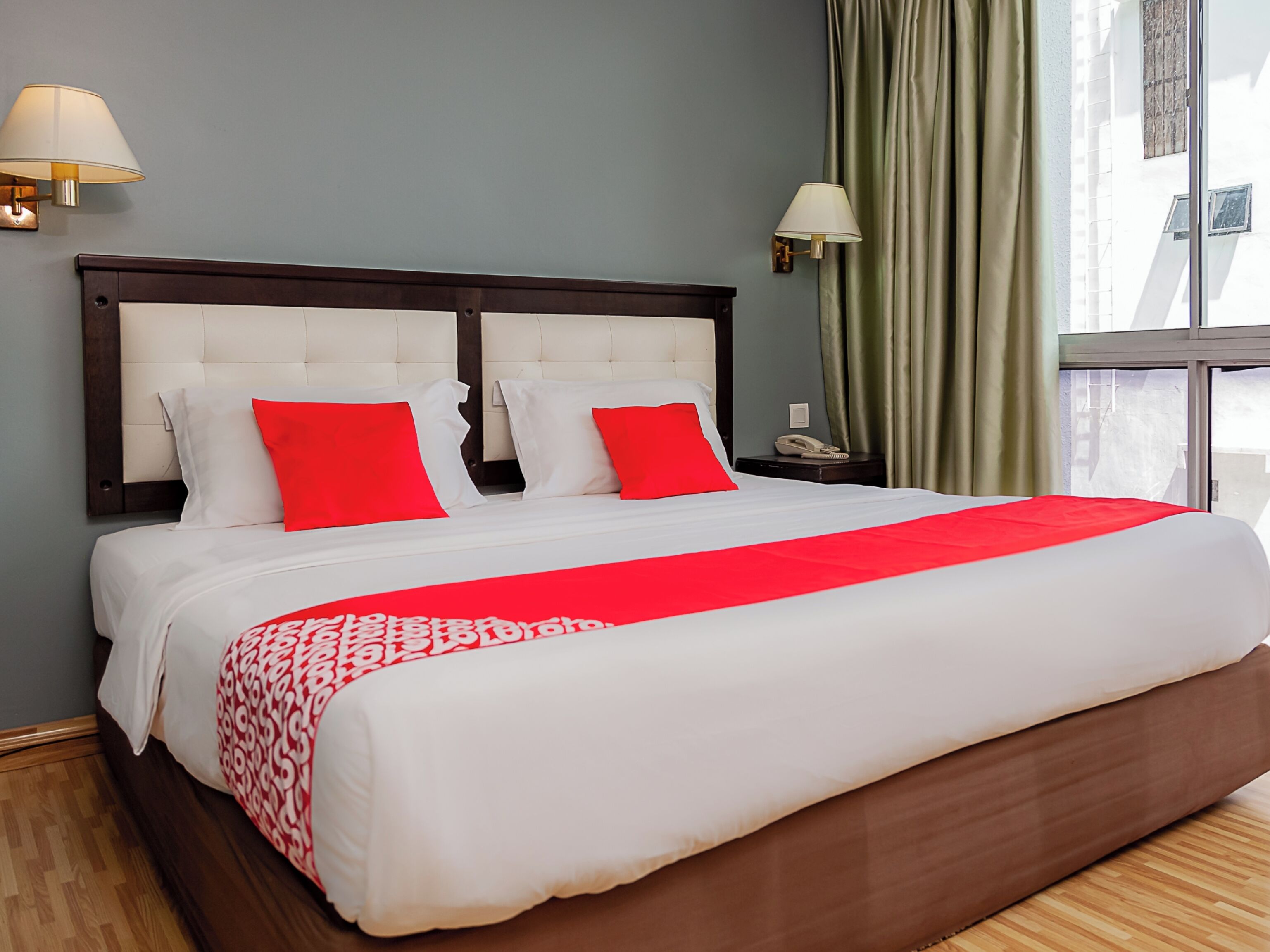 A hotel room with a large bed, two bedside lamps, a telephone, and a window with curtains.