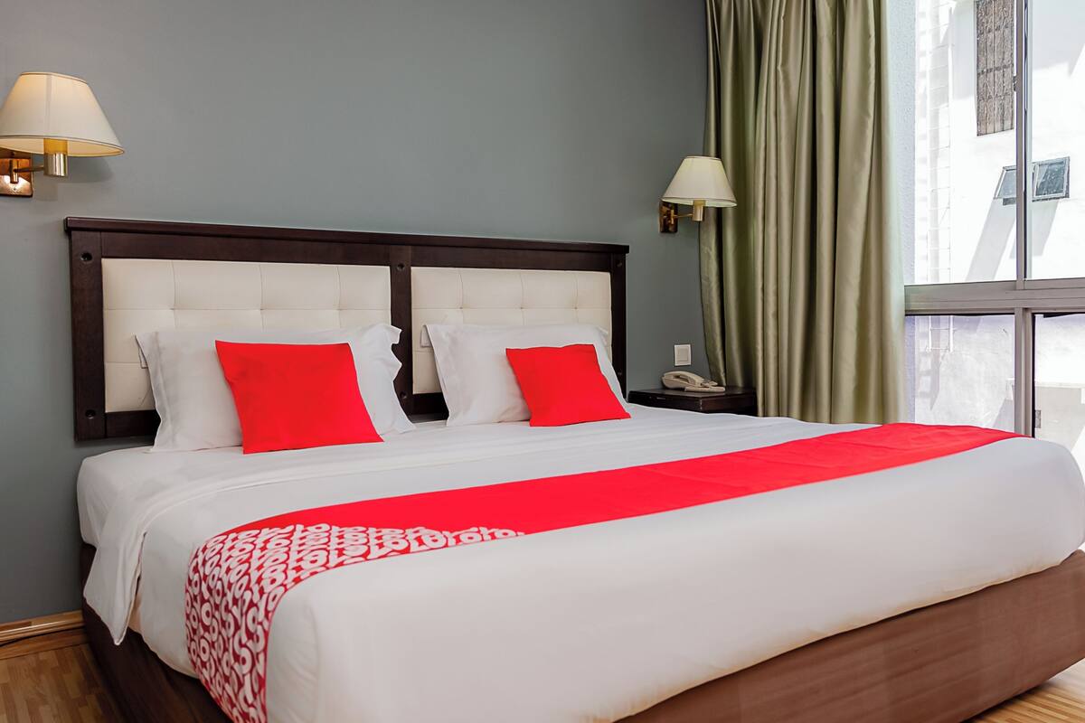 A neatly made bed with white and red bedding, a wooden headboard, and two bedside lamps.