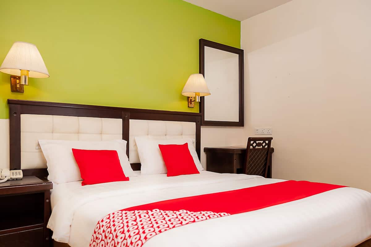 A hotel room with a bed, two bedside tables, a nightstand, a chair, and a mirror on the wall.