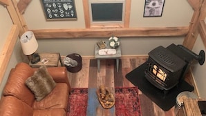 Een knus interieur met een leren bank, een rood tapijtbalkmat, een houten salontafel, een klein bijzettafeltje met een lamp, een lijst met een afbeelding en een houtkachel.