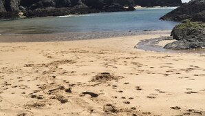 Ein sandiger Strand mit Felsformationen und ruhigem Wasser.