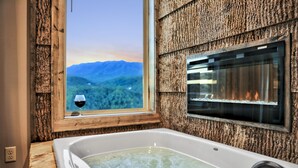 Ein Badezimmer mit einer Badewanne, einem Fenster mit Bergblick und einem Weinglas auf der Fensterbank.
