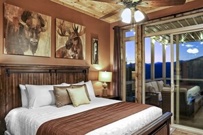 A bedroom with a wooden headboard, a large bed with white and brown bedding, two paintings of bulls on the wall, a nightstand with a lamp, and a sliding glass door leading to an outdoor seating area.