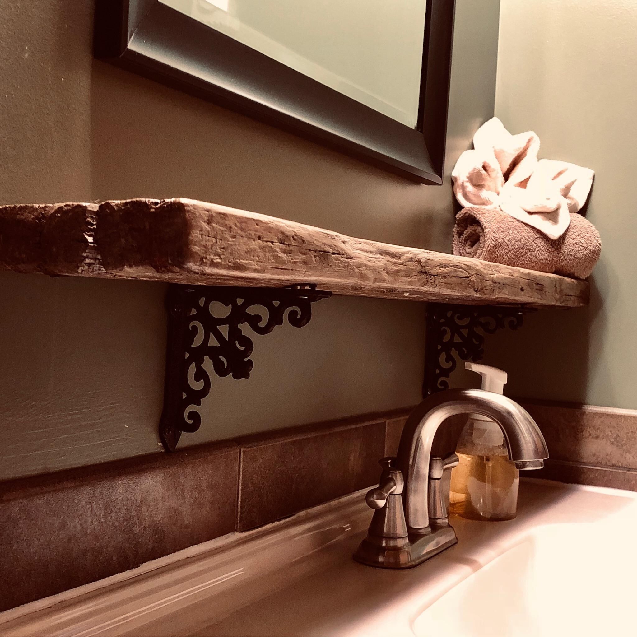 A bathroom with a wooden shelf holding a towel, a sink with a faucet, and a mirror above the shelf.