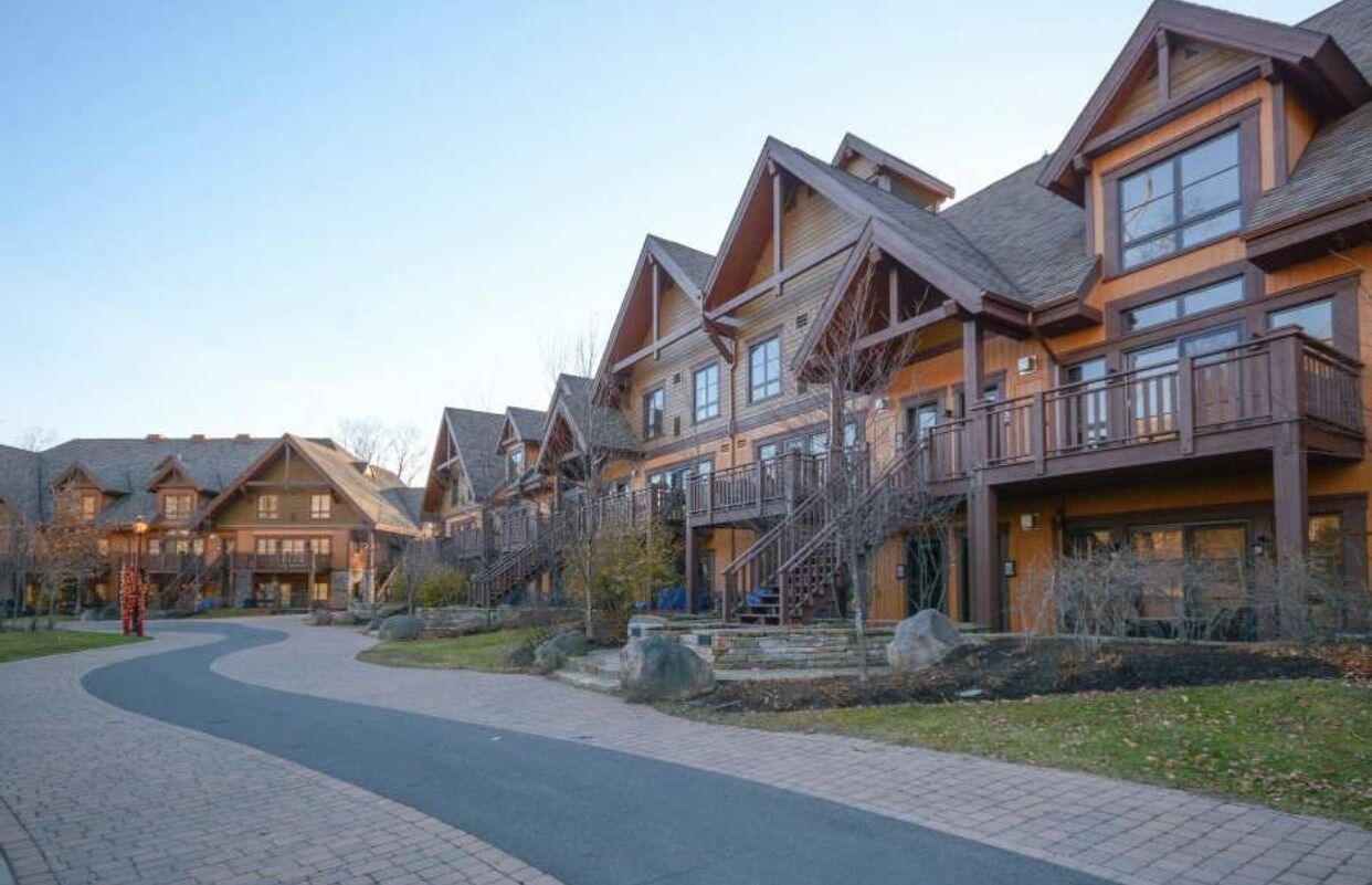 A row of log cabin-style buildings with multiple stories, balconies, and a paved walkway.