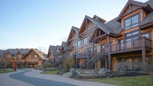 A row of log cabin-style buildings with multiple stories, balconies, and a paved walkway. - SPECTACULAR SKI IN - SKI OUT Golf Hiking Biking Casino Chalet in Mont Tremblant  (Mont-Tremblant)