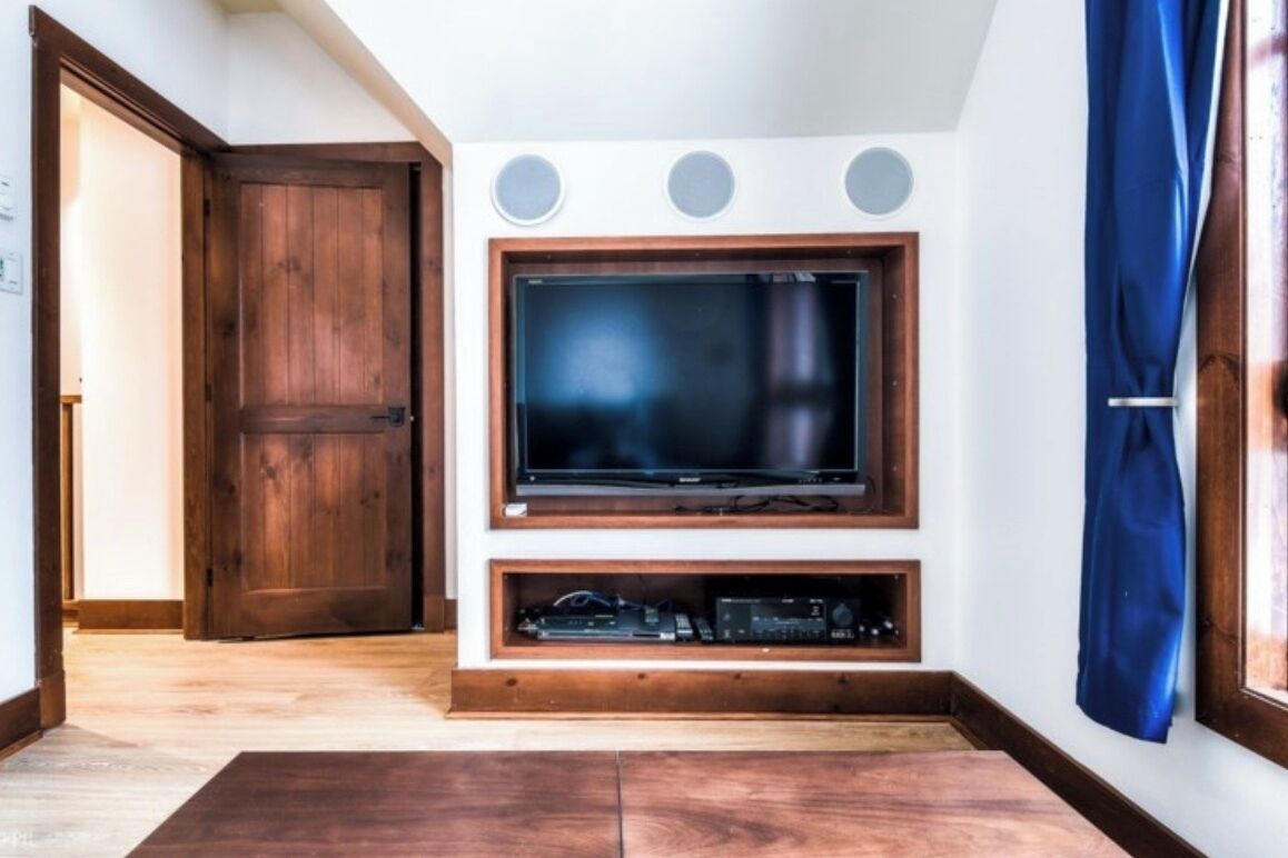 Una sala de estar con un televisor de pantalla plana grande montado en una pared de madera, una puerta de madera y una ventana con cortina azul.