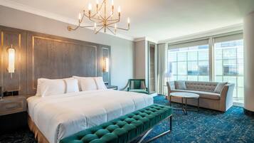 A hotel room with a large bed, a green upholstered bench, a round coffee table, a sofa, and a chandelier.