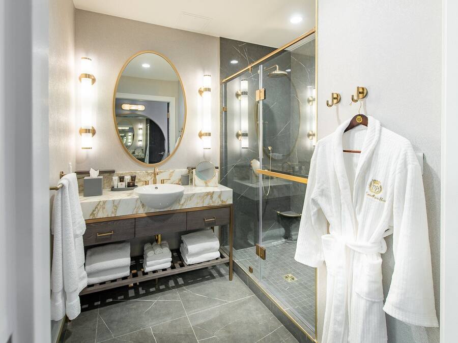 Une salle de bain moderne avec un meuble-lavabo en marbre, un grand miroir, une douche à parois de verre et un peignoir suspendu à un porte-serviettes.