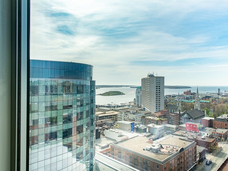 A high-rise building with a glass facade overlooking a cityscape with a body of water and a distant island.