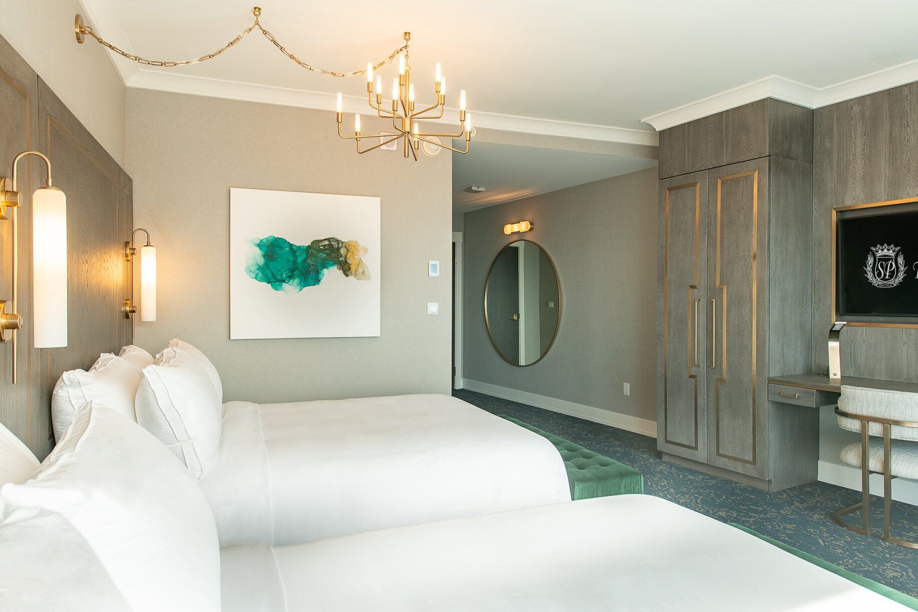 A hotel room with two beds, a chandelier, a mirror, and a wardrobe.