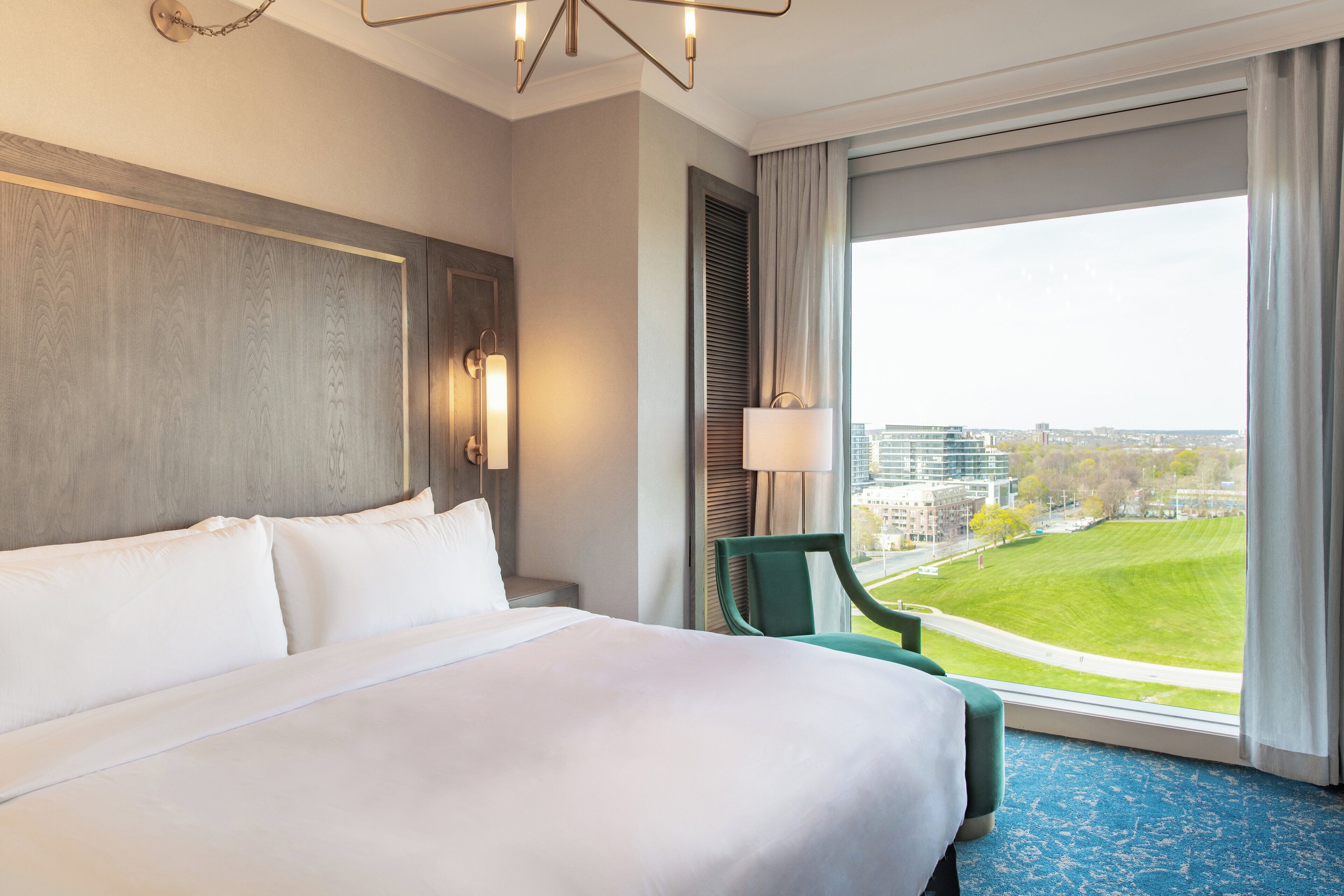 Ein Hotelzimmer mit einem großen Bett, Blick auf die Stadt und einem grünen Sessel am Fenster.