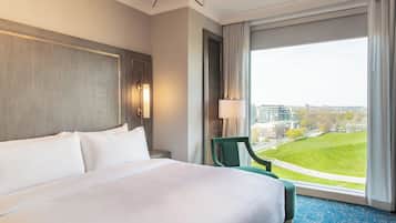 Quarto de hotel com uma cama grande, vista para a cidade e uma cadeira verde perto da janela.