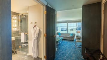 A hotel room with a glass-enclosed shower, a robe hanging on a hook, a bed with a blue carpet, and a seating area with a sofa and chairs.