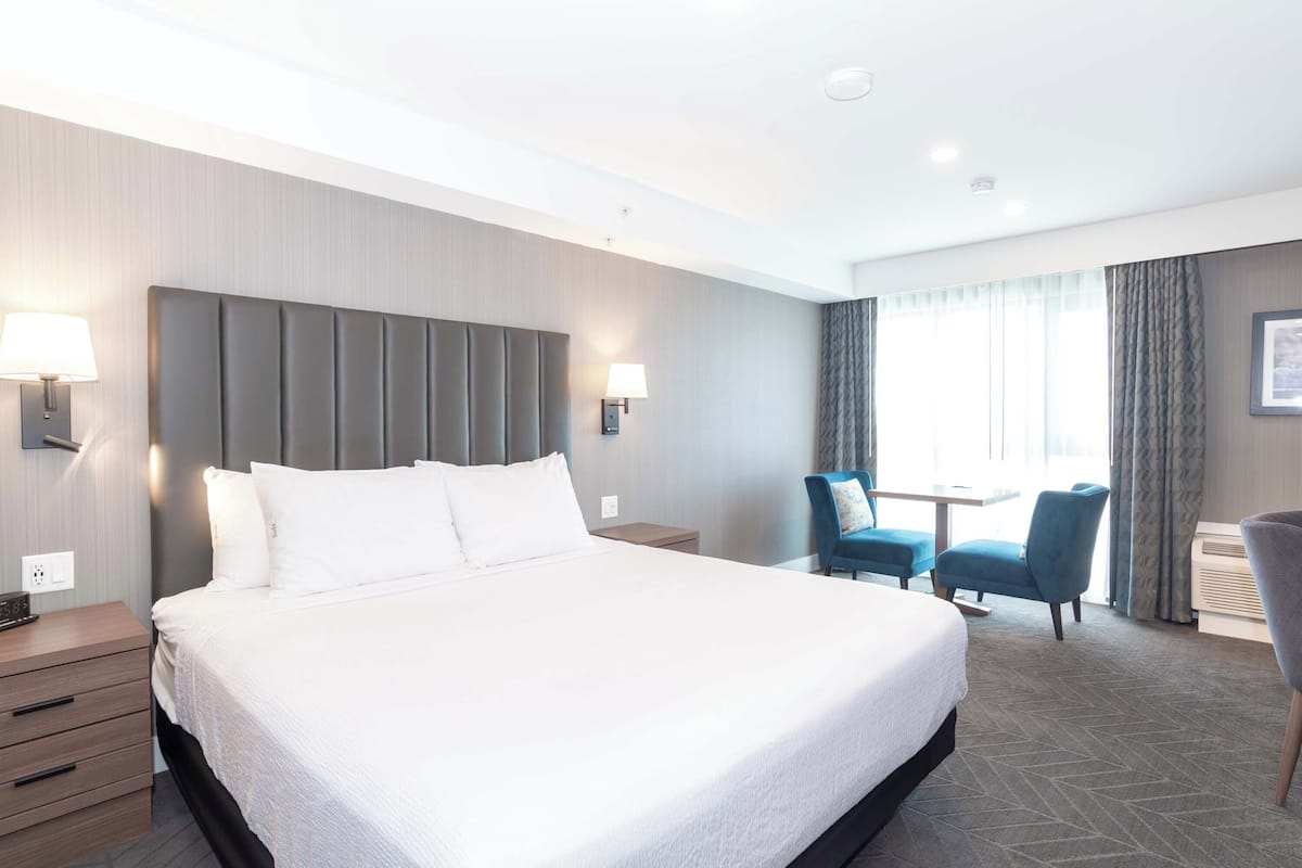 Habitación de hotel con una cama grande, lámparas de noche, un escritorio con una silla y vistas al exterior.