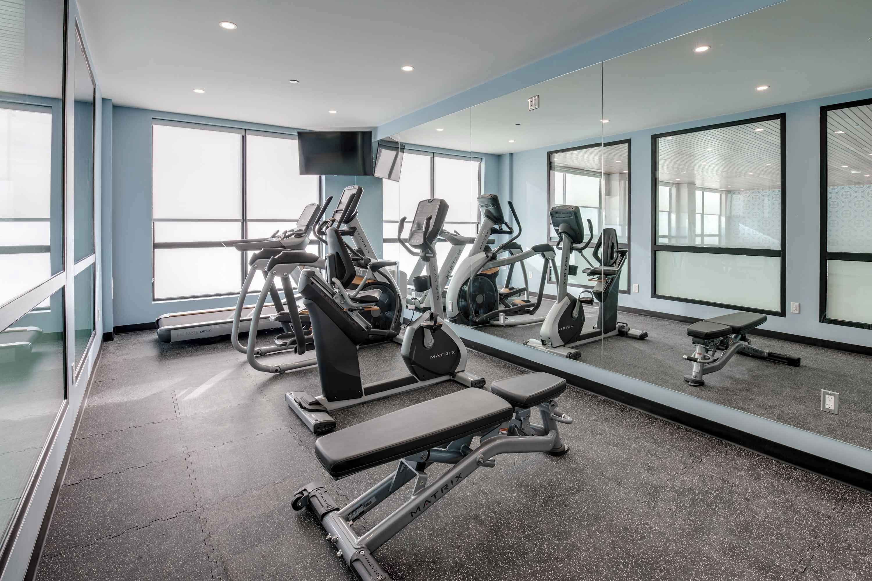 A gym with cardio machines, weight benches, and mirrors.