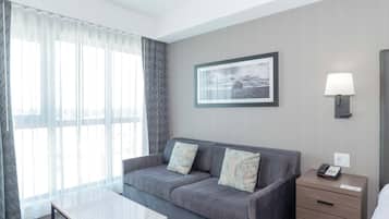 A hotel room with a grey sofa, a small table, a lamp, and a framed picture on the wall.