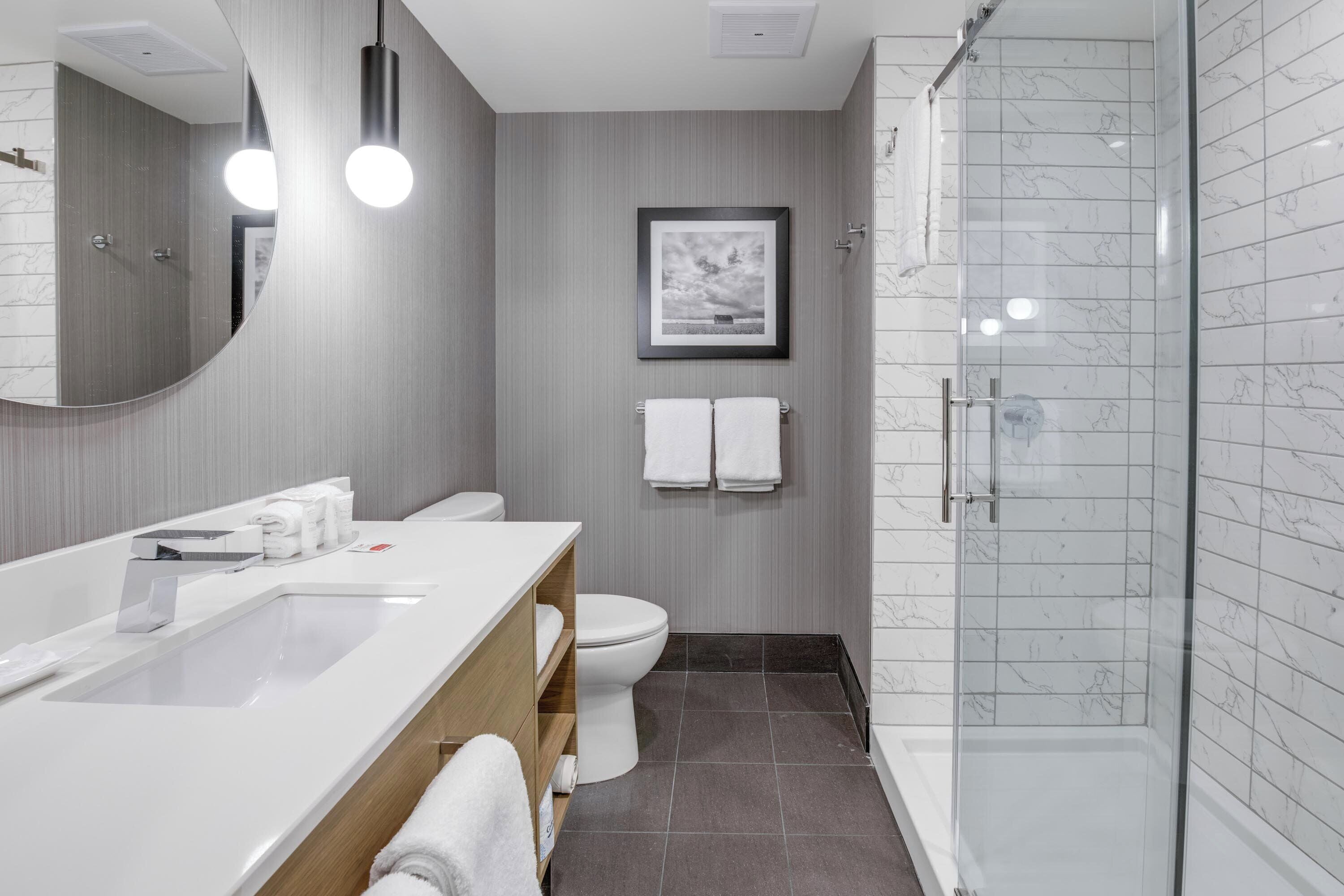 A modern bathroom with a large mirror, white sink, toilet, and a glass-enclosed shower.
