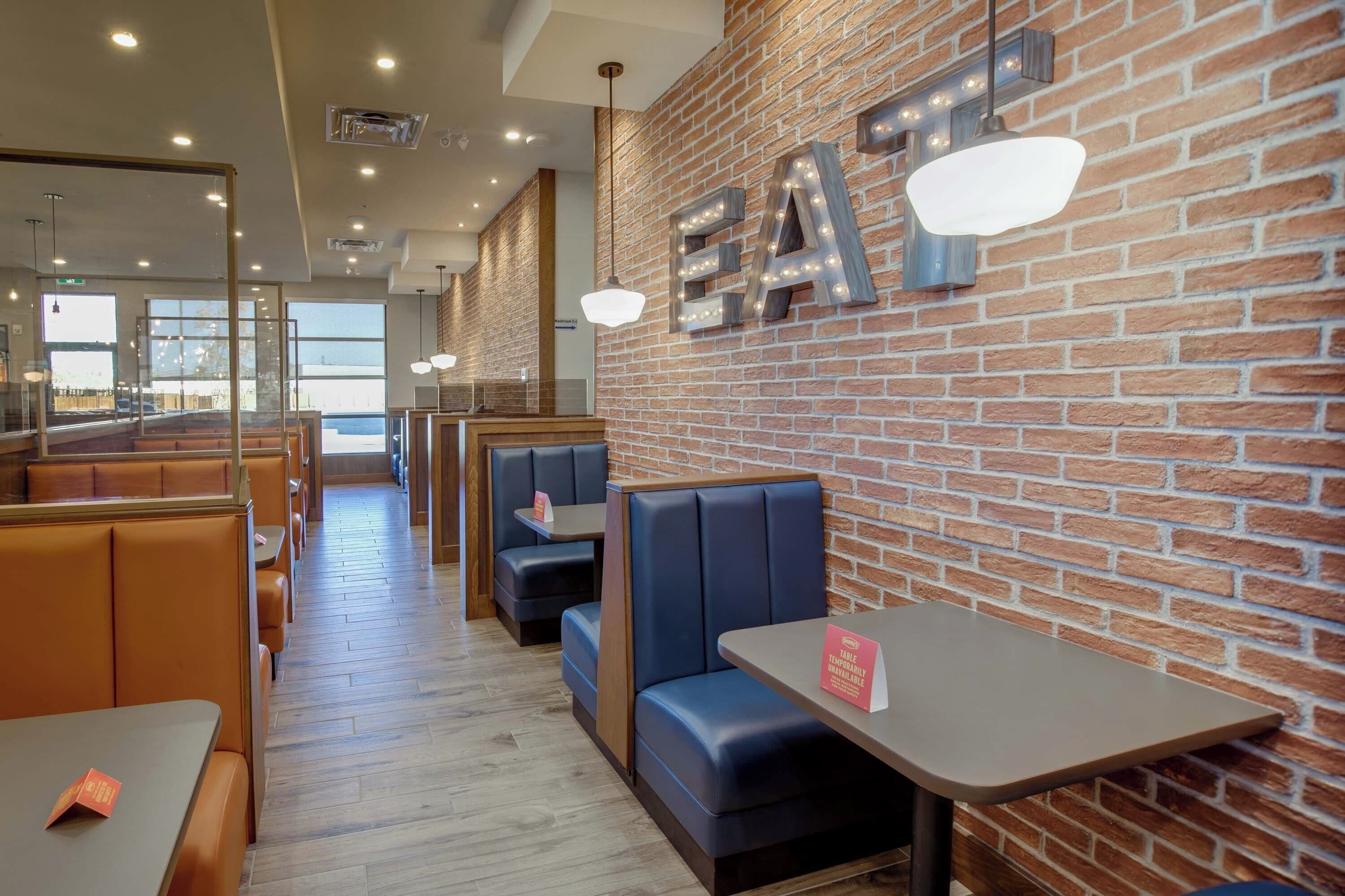 A restaurant interior with brick walls, seating areas, and illuminated signage.