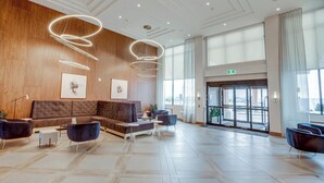 A spacious lobby with a large brown sofa, two armchairs, a coffee table, and a modern light fixture. - Sandman Signature Saskatoon South Hotel (Saskatoon)