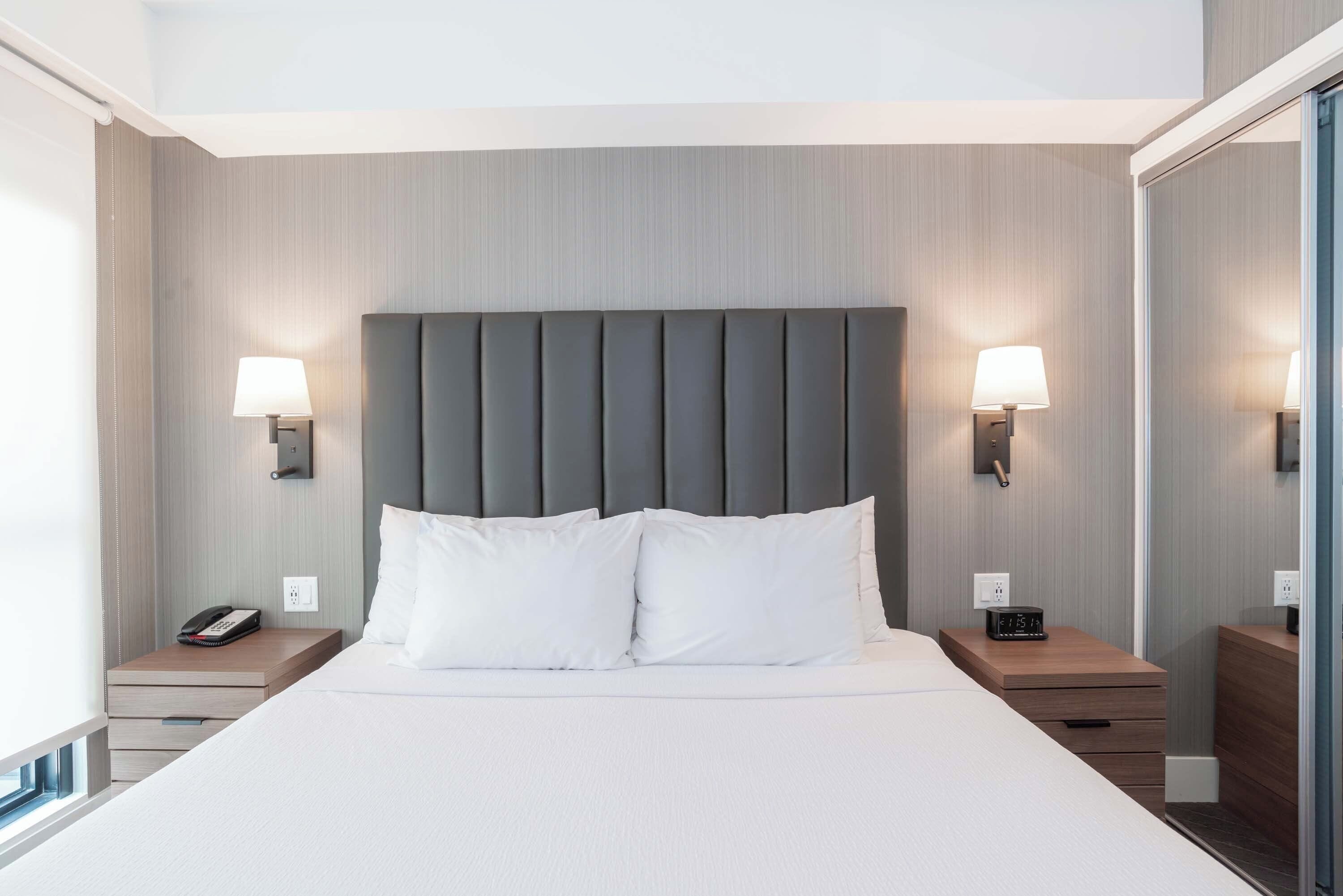 Una habitación de hotel moderna con una cama grande, dos mesitas de noche, una lámpara de pared y un teléfono en una de las mesitas.