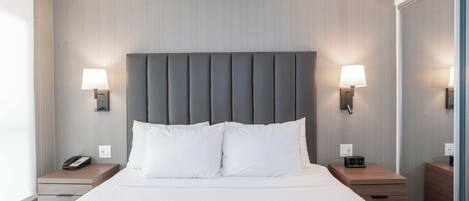 A modern hotel room with a large bed, two bedside tables, a wall-mounted lamp, and a telephone on one of the tables.