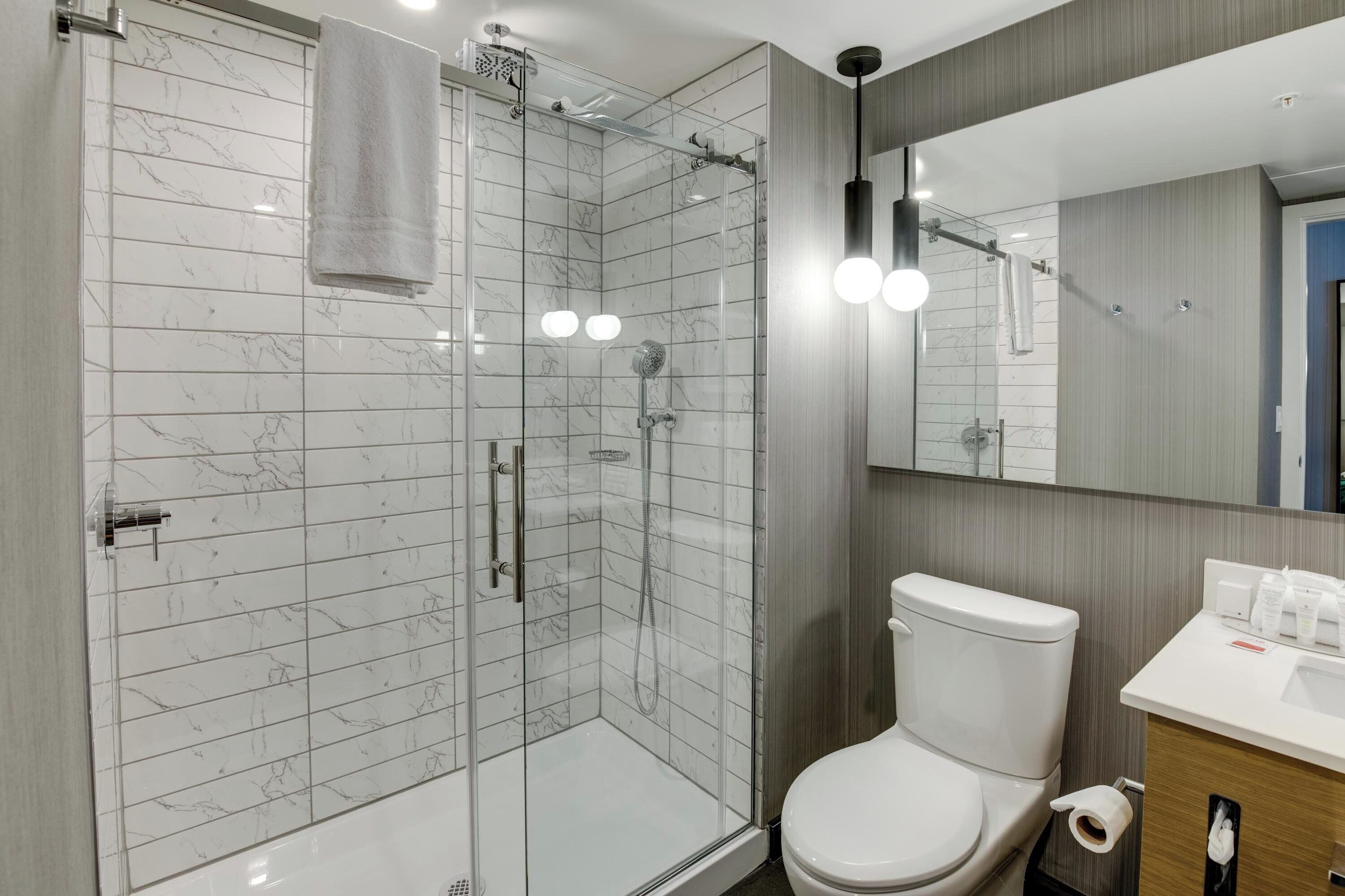 A modern bathroom with a glass-enclosed shower, a white toilet, and a wooden vanity with a mirror.