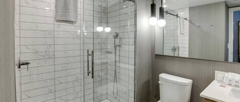 A modern bathroom with a glass-enclosed shower, a white toilet, and a wooden vanity with a mirror.