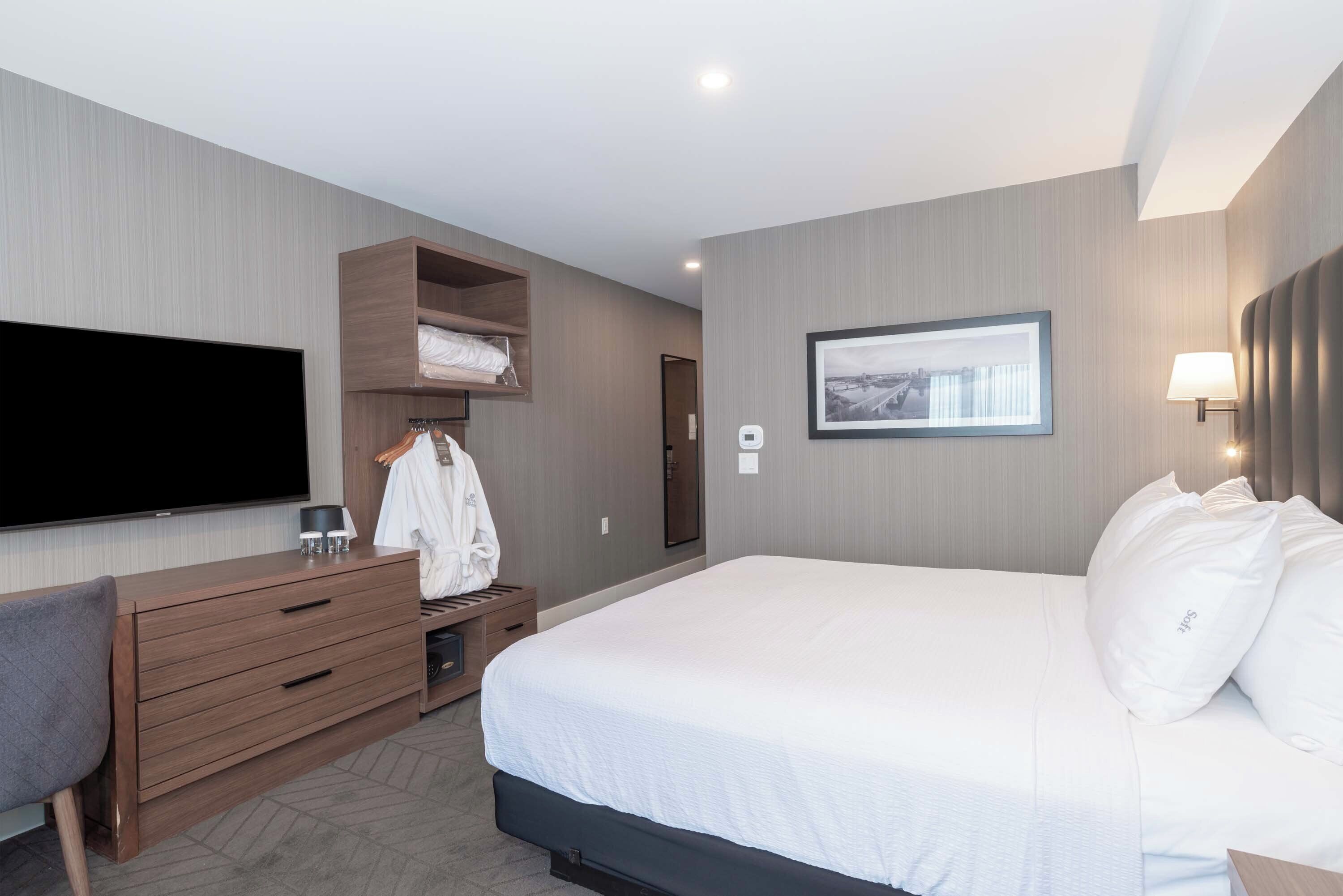 A hotel room with a large bed, a flat-screen TV, a wooden dresser, and a wardrobe.