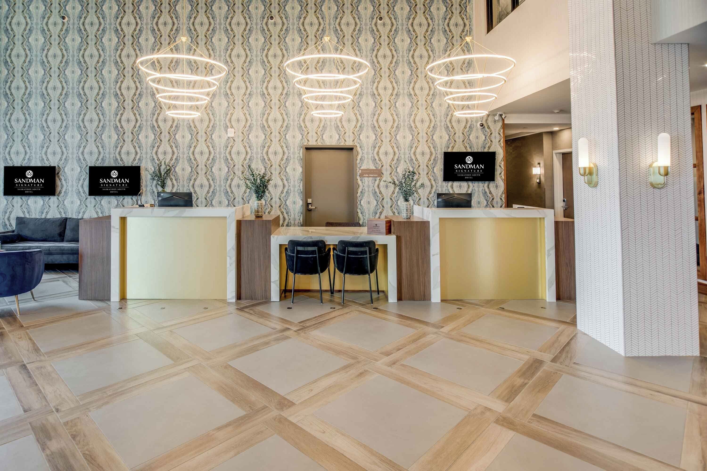 Zona de recepción de hotel con diseño moderno, que incluye un papel tapiz estampado, un mostrador de recepción con dos sillas y un espejo grande sobre el mostrador.