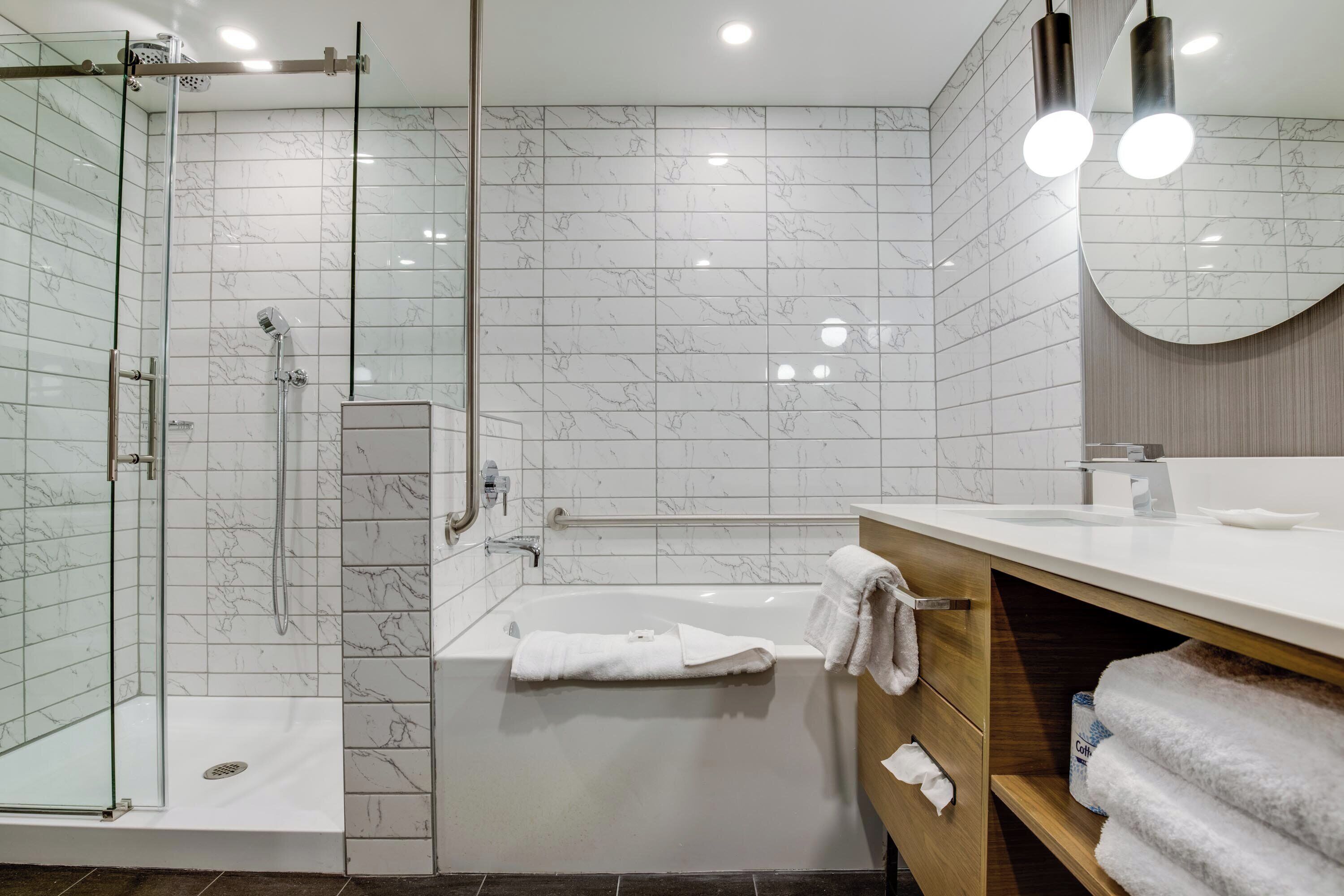A modern bathroom with a glass shower enclosure, a freestanding bathtub, and a vanity with a mirror.