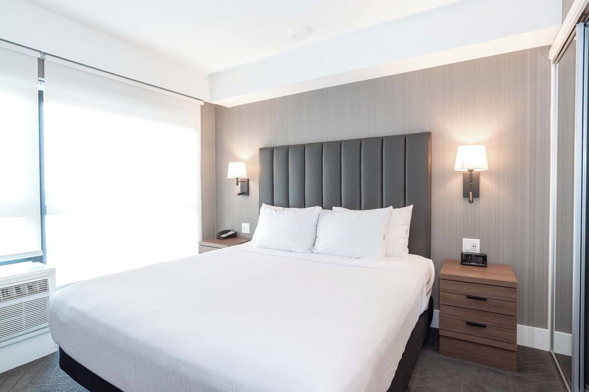 Una habitación de hotel moderna con una cama grande, lámparas de noche, una mesita de noche y una ventana con persianas.