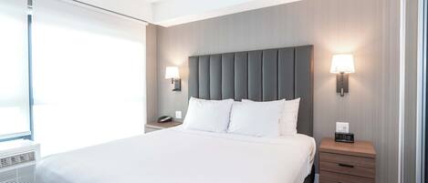 A modern hotel room with a large bed, bedside lamps, a nightstand, and a window with blinds.
